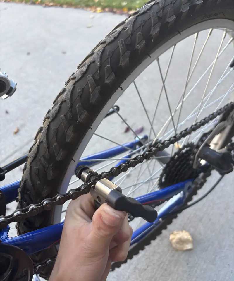 A chain tool clamped on the chain of a blue mountain bike, rear cassette behind it.